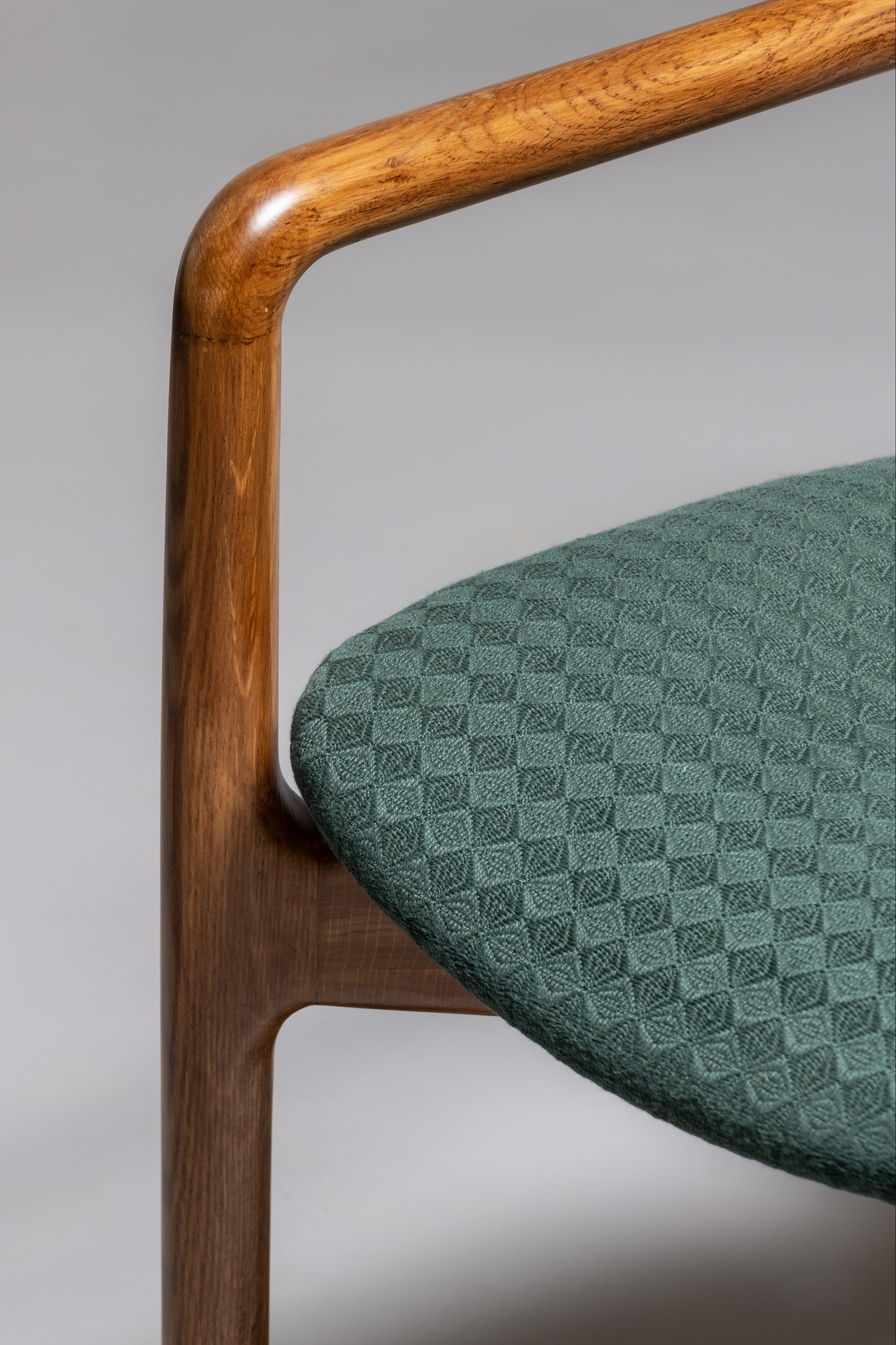 Chair with wooden armrest and green patterned seat on a gray background