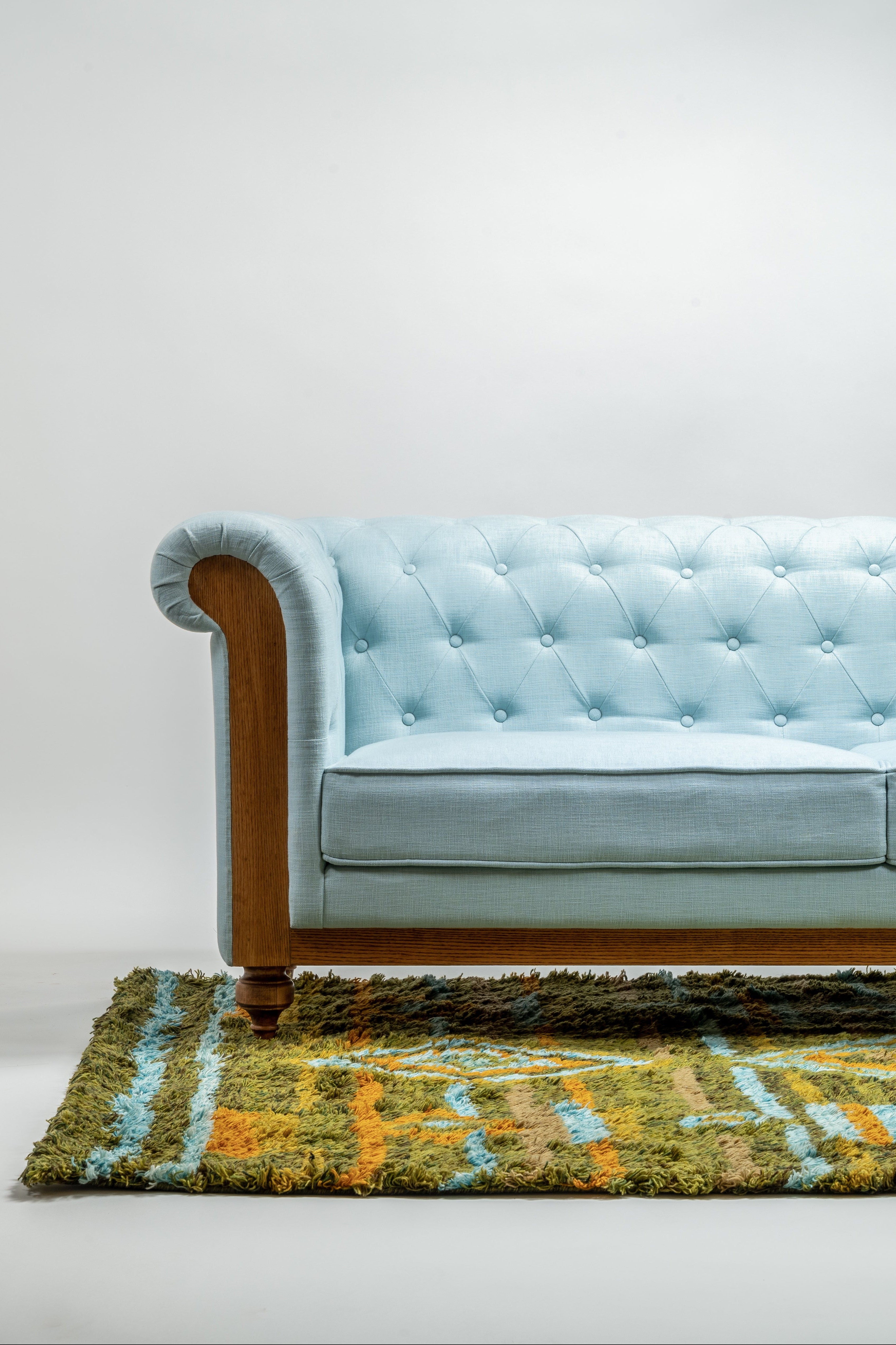 Light blue tufted sofa with wooden legs on a white background